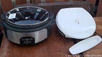 General Electric slow cooker on left with glass lid and George Foreman white electric grill on right with power cord and drip tray in front.