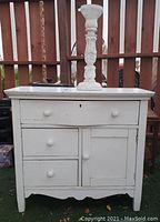 Front view of white antique 4 drawer cabinet and tall wood candle holder showing design and knobs.