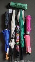 Overview of eleven assorted umbrellas in various colors and closed state, showing handles and sleeves