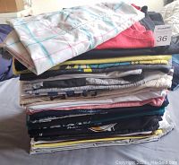 Stack of 25 folded men's and boys' T-shirts in assorted colors and styles, showing variety of brands.