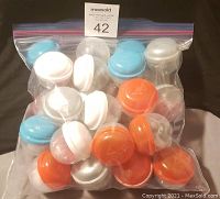 A sealed plastic bag containing mini fitted hats with mostly white crowns and colored brims and button tops in blue, white, and orange colors, showing the lot in its packing state.