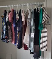 Full rack view showing 15 various women's blouses and jackets hanging on a rod, arranged side by side with various colors and patterns visible.