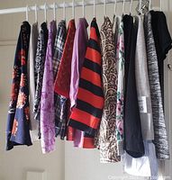 Photo of fourteen women's long sleeve blouses hanging on rack showing variety of colors and prints including floral, plaid, stripes, and solids.