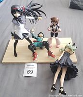 Four anime figurines positioned on a wooden stand and fabric surface, showing scale and condition.