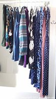 Twelve women's clothing pieces hung on a rack showing an assortment of jumpers, pants, and dresses in various prints and colors.