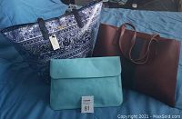 Three items shown together: blue patterned Soma tote with button closure, brown open tote bag, and light green iPad case.