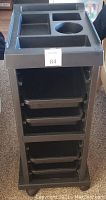 Front view of black rolling salon trolley with molded top compartments and 4 removable trays stacked vertically.