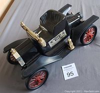 Angle view showing front and side of the black car-shaped whiskey bottle with red wheels and gold-tone accents, label visible