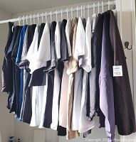 Twenty-two pieces of men's clothing including predominantly t-shirts and jackets hanging on a white rod, showing assorted colors and sizes.