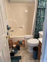 Wide view of bathroom showing bathtub, toilet, shower, and storage items on the floor near toilet