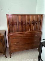 Front view of walnut two-piece chest showing carved geometric doors and three-drawer base