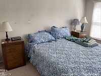 Bedroom scene showing the pair of wooden nightstands positioned beside a bed with blue patterned bedding.
