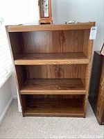 Front view of the MDF bookcase showing three shelves and woodgrain finish with some scratches.