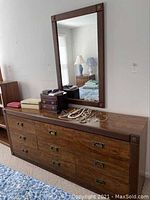 Full view of wood dresser with nine drawers and various items on top, reflecting light in the mirror above.