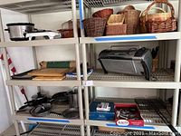 Wide view of shelves with crockpot, woven baskets, toaster oven, cutting boards, cookware and boxed games.