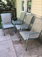 Four outdoor patio chairs placed on concrete patio against house wall showing seating surfaces and chair frames