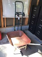 Photo showing green metal moving dolly and the rusted wheelbarrow positioned in a storage area.