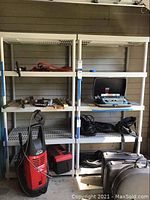 Photo showing two white plastic shelving units with grid surfaces, items stored but not included, placed in a garage environment