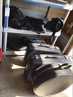 Three black American Tourister hard-sided suitcases with tri taper design placed on the floor, with shelves above holding four soft-sided black bags