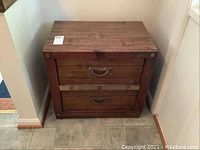 Front view of wooden cabinet with two drawers and bronze tone handles. Cabinet shows some scratches and wear.