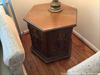 Front angle view of hexagonal side table showing wood top, door with decorative hardware, and storage space below.