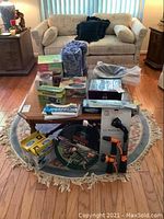 Full view of the lot on a living room coffee table and rug showing various boxed and unboxed household and kitchen items