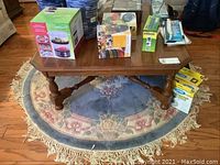 Wood square coffee table on a round floral rug with items placed on top but not included in the lot