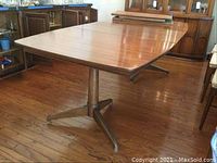 Full view of the rectangular mid-century modern wood dining table with pedestal metal legs and three-point base, showing the table's general condition and shape.