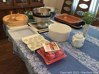 Photo of assorted serving dishes including bowls, egg trays, egg poaching molds, roasting pan, placemats, and teapot on a blue floral tablecloth.