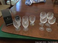 Nine Waterford crystal stemmed glasses displayed on table with one original Waterford box visible. Five smaller glasses in front, four larger wine glasses behind.