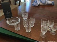 Photo showing all Waterford crystal items including ashtray, stemmed glasses, additional glasses, and empty Waterford box on a wooden surface.