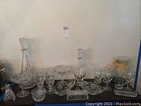 Full overview of the lot showing two glass decanters, multiple footed candy dishes, bowls, stemmed glasses, and a footed vase with a raffia bow.