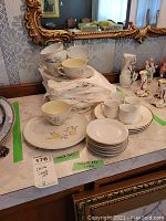 Set of seven snack cups and matching plates stacked on a marble surface with ornate mirror background, showing pastel floral designs and gold rims.