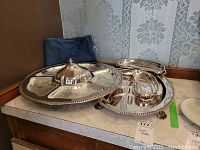 Overview of the silverplate serving set including sectioned server with removable lid, glass inserts, side servers, and felt bags.