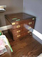 Photo of one Kroehler 3-drawer wooden side table with brass handle accents on dark wood flooring against gray wall, shows minor wear on top and surface.