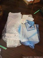 Vintage embroidered and embossed tablecloths folded and bagged on floor with white and blue colored linens visible