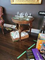 Full front view of carved round side table with glass top, decorative glassware visible on surface