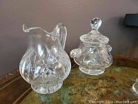 Creamer and sugar bowl with lid on a glass table, showing faceted crystal pattern and solid bases.