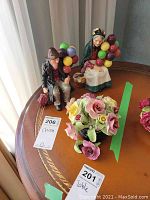 Photo showing both Royal Doulton figurines of the Balloon Man and the Old Balloon Seller seated with colorful balloons, alongside the floral porcelain piece.