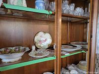 Cabinet shelf showing multiple porcelain items including the Love Story bowl at center and cake plate on left.