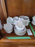 Photo of stacks of 12 teacups and 12 matching saucers, white porcelain with pink cherry blossom design and gold trim.