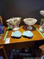 Image of Italian handmade pedestal dish with open lattice bowl, fan-shaped vase with detailed gold leaf accents, and two pale blue Carlton Ware leaf-shaped dishes with gold trim on wooden table