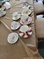 Lot of seven unique vintage teacup and saucer sets arranged on a table covered with brown paper