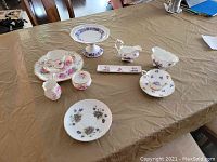 Photo depicting all tea set items arranged on a table including teacups, saucers, plates, cream and sugar set, mint dish, and footed compote.