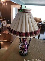 Full view of the vintage urn style ceramic lamp with pleated ruffled shade on a table.