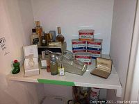 Wide view photo showing various perfume bottles and coffee tins arranged on a white shelf, including boxed perfumes and decorative bottles