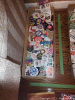 Top-down photo showing a large collection of vintage buttons and pins packed in a box on a wooden surface next to a couch.