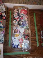 Wide shot of cardboard box filled with more than 30 assorted vintage buttons and pins with various slogans, colors, and designs.