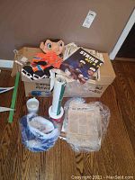 Mixed items in box with doll, poster, badges, and a mug on floor