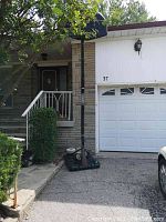 Portable basketball hoop standing upright on driveway near stairs and garage, with black pole and base filled with weight.